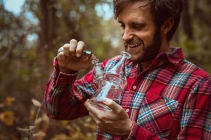 man in the woods smoking cannabis out of a bong